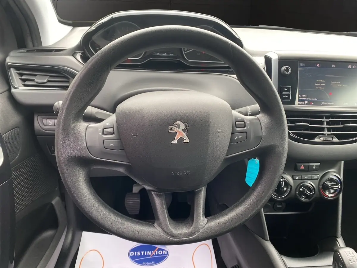 Vue intérieure centrée sur le volant Peugeot 208 noir avec tableau de bord et écran tactile à droite.