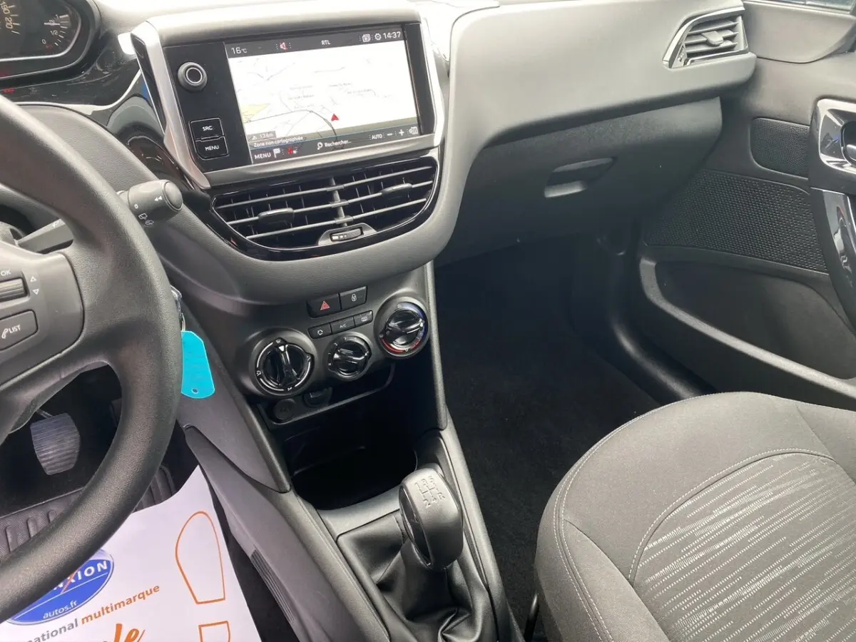Vue intérieure côté conducteur de la Peugeot 208 Affaire noire, avec tableau de bord tactile et levier de vitesses manuel.