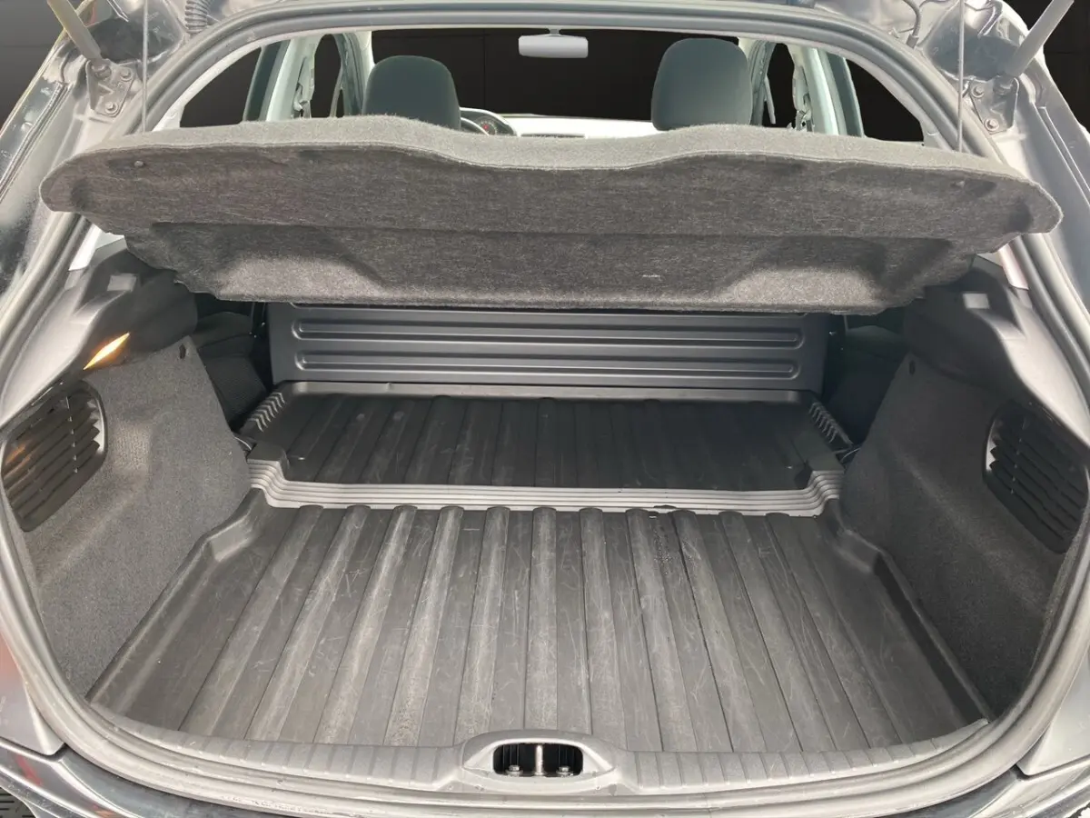 Coffre ouvert vu de l'arrière d'une Peugeot 208 Affaire noire, montrant l'espace de chargement avec tapis en caoutchouc.