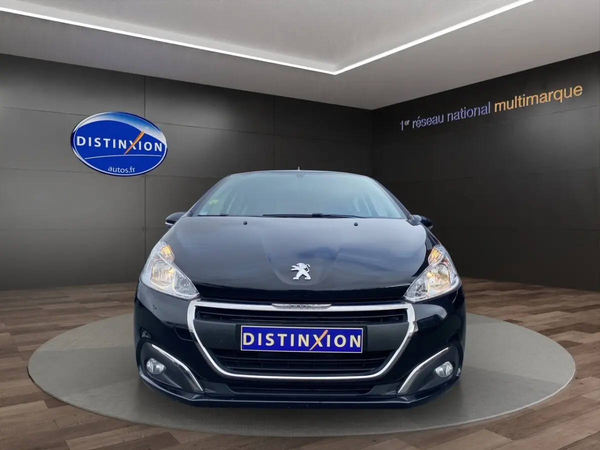 Vue frontale d'une Peugeot 208 AFFAIRE noire, avec phares allumés et calandre chromée dans un showroom.