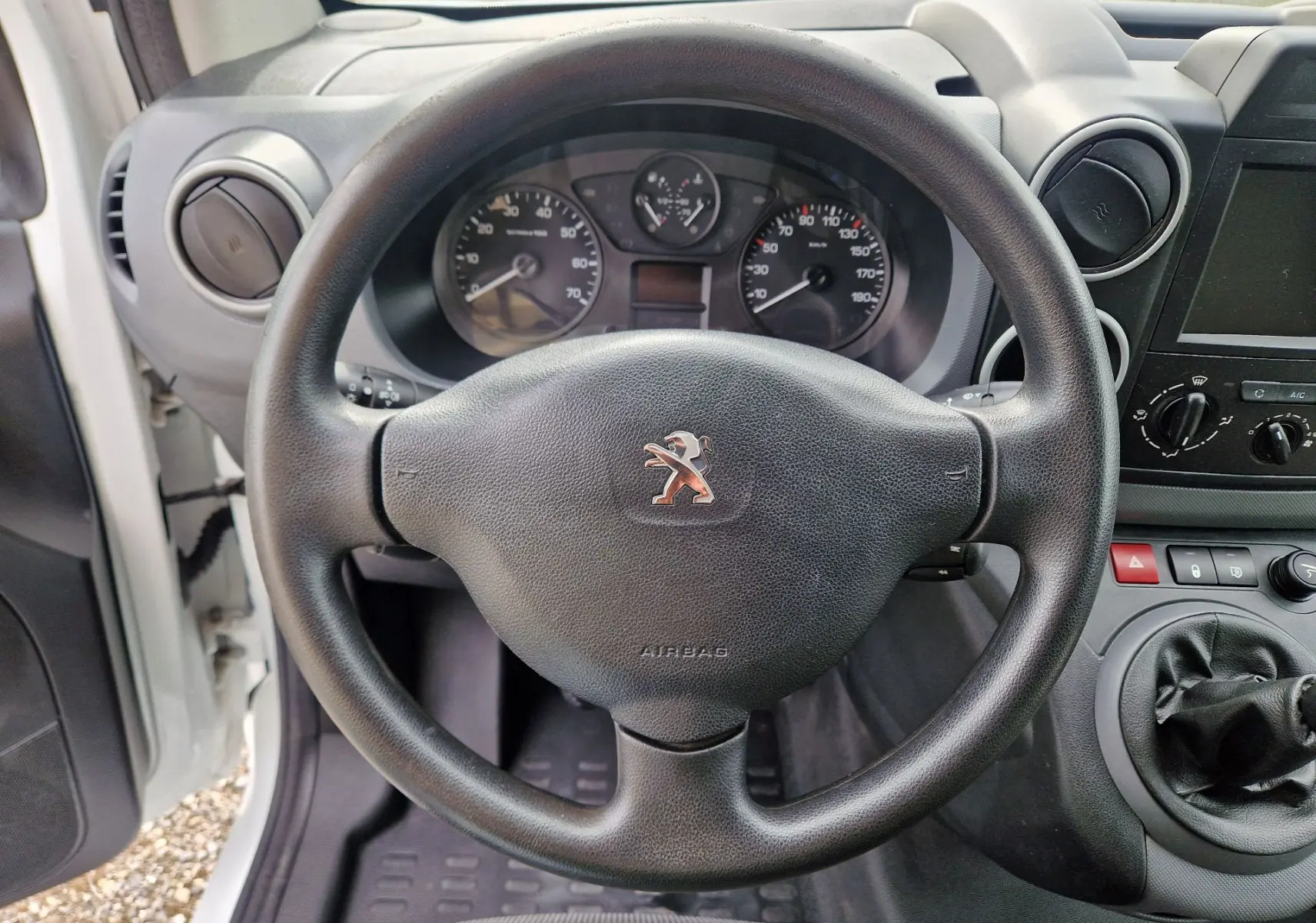 Vue rapprochée du volant noir et du tableau de bord du Peugeot Partner blanc, avec levier de vitesses manuel visible.