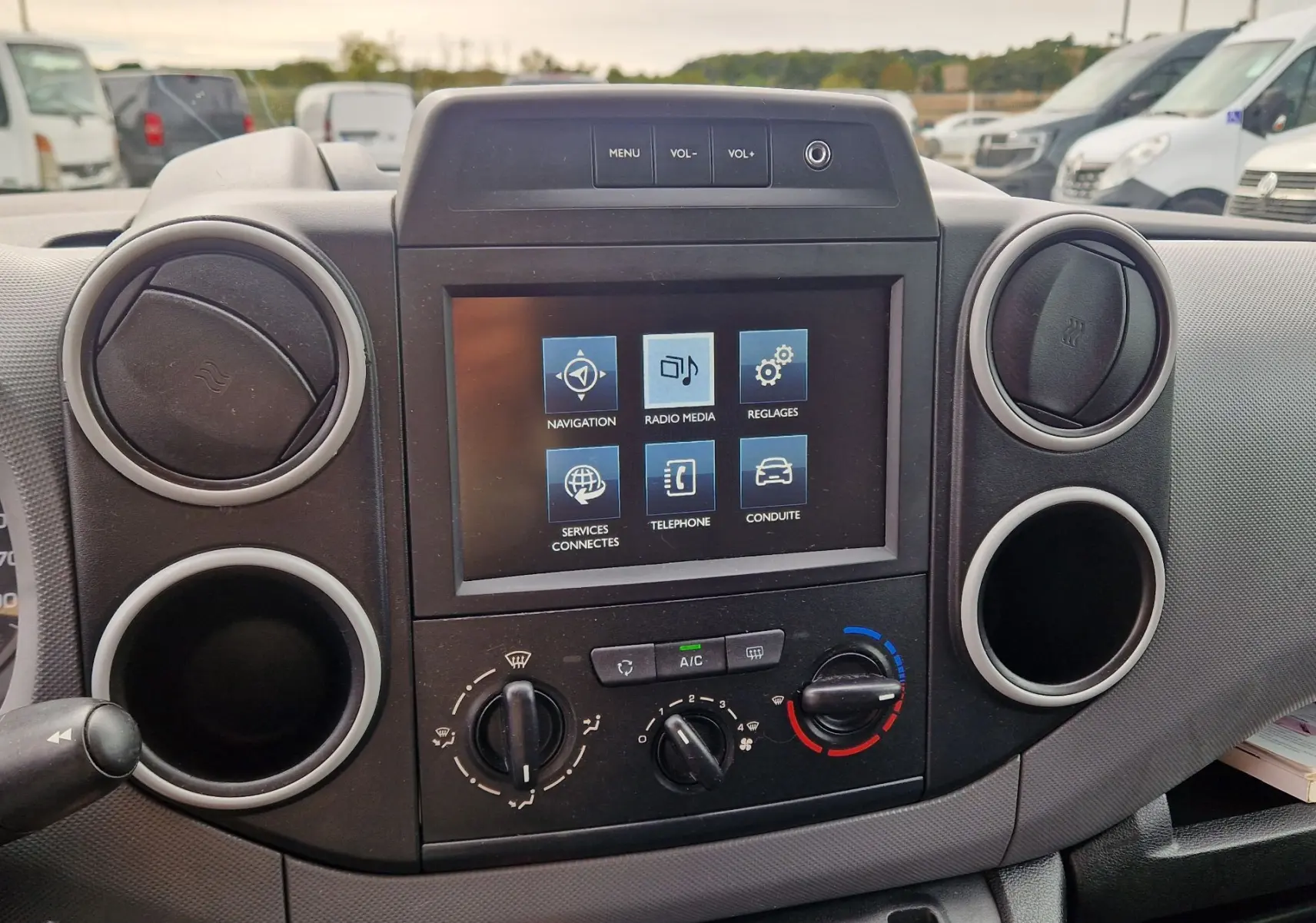 Vue rapprochée du tableau de bord du Peugeot Partner blanc, mettant en valeur l’écran tactile et les commandes de climatisation.