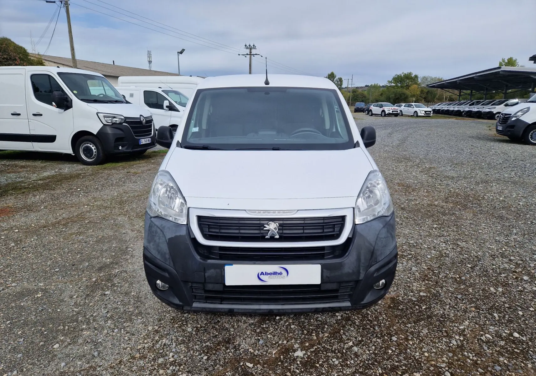 Vue de face d’un Peugeot Partner blanc de 2017 avec pare-chocs avant noir et calandre distinctive sur un terrain gravillonné.
