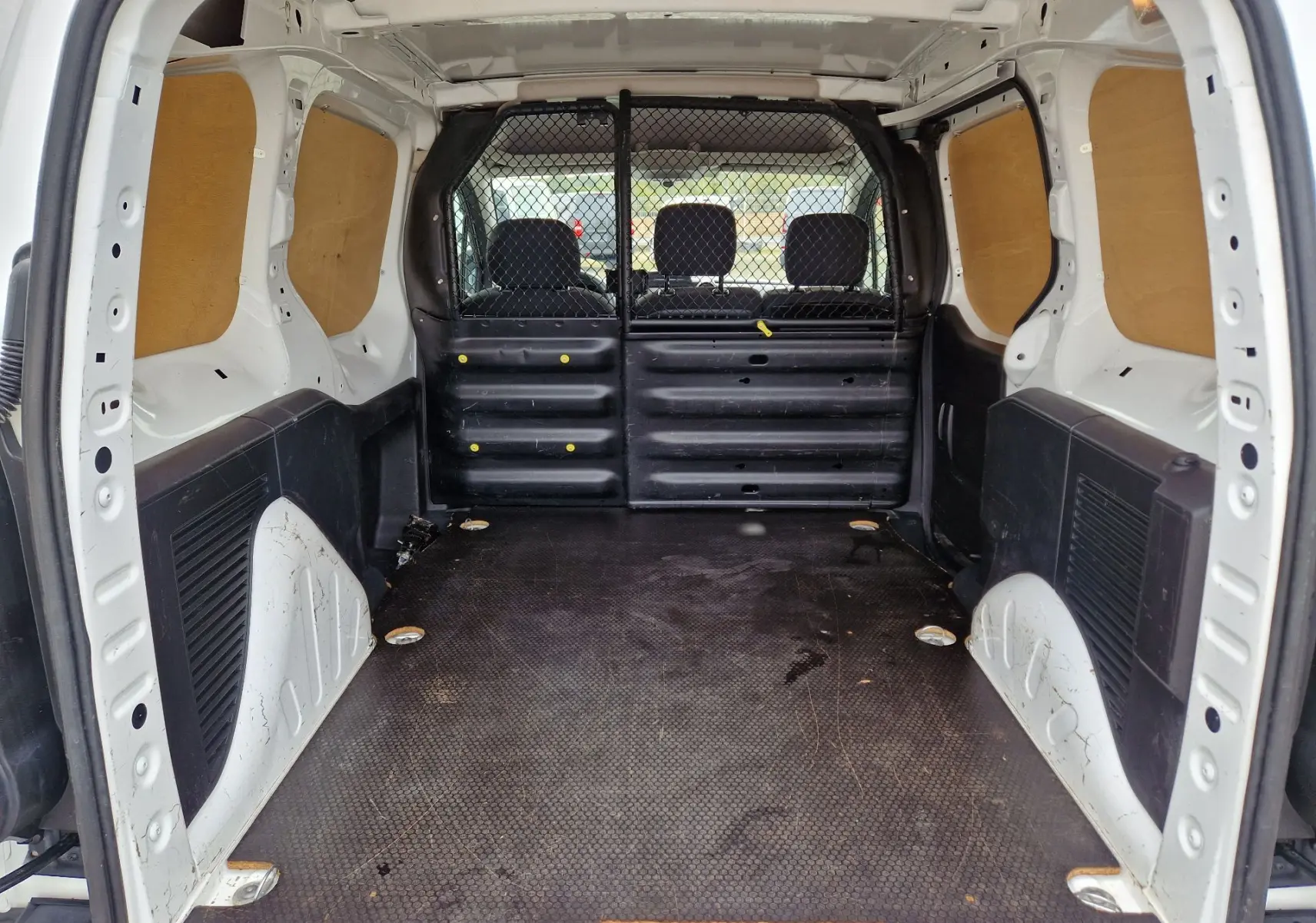 Vue intérieure arrière du Peugeot Partner blanc 2017, montrant l’espace de chargement avec cloison grillagée et panneaux bois latéraux.