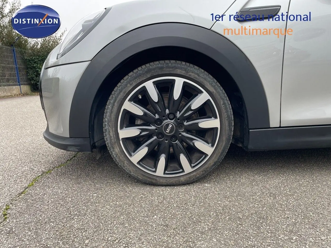 Gros plan sur la roue avant gauche d'une MINI 1.5 136CH STEPTRONIC 2023 couleur Melting Silver Metal avec jante bi-ton noire et argent.