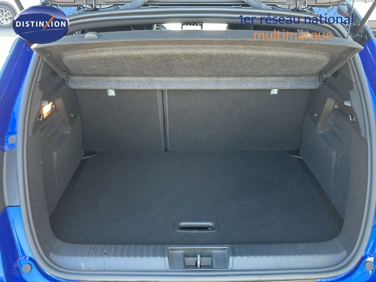 Coffre ouvert d'un Renault Captur E-Tech hybride 2025 bleu iron metal avec toit noir, vue arrière en extérieur.