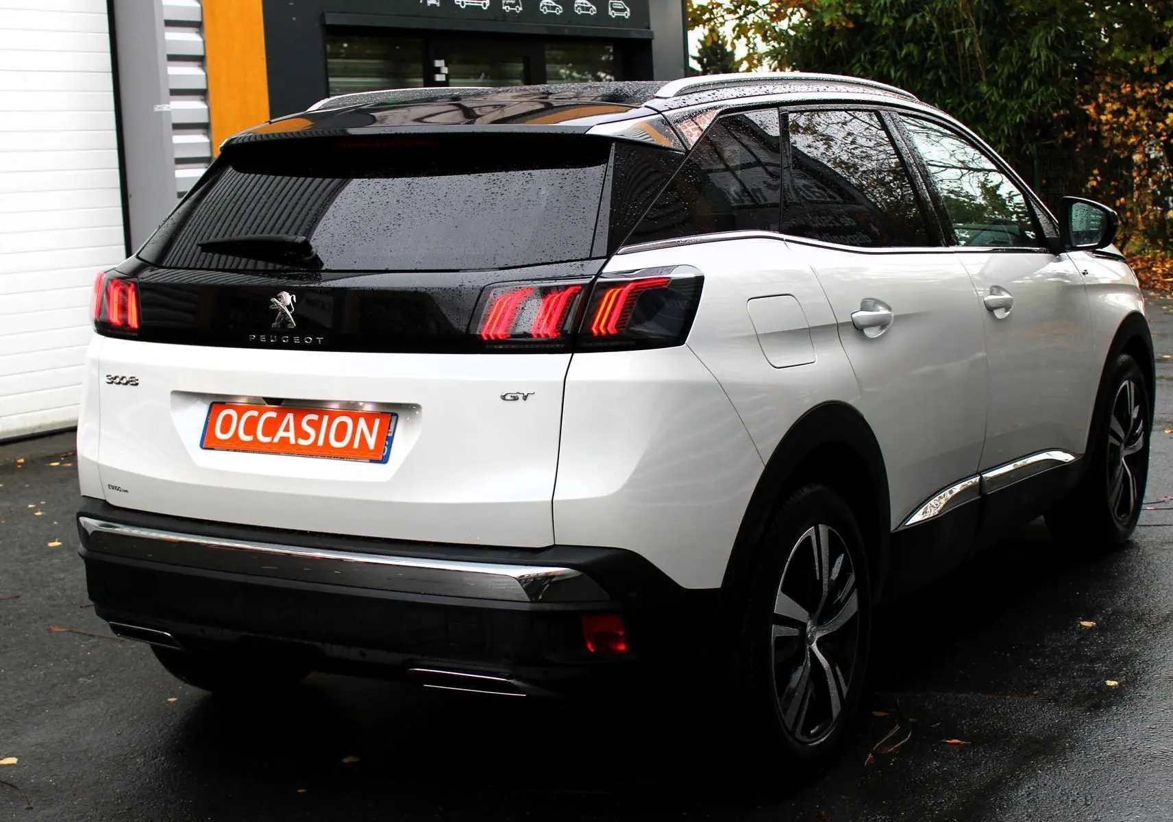 Vue 3/4 arrière droite d'un Peugeot 3008 blanc nacré avec toit panoramique noir et feux arrière LED distinctifs.