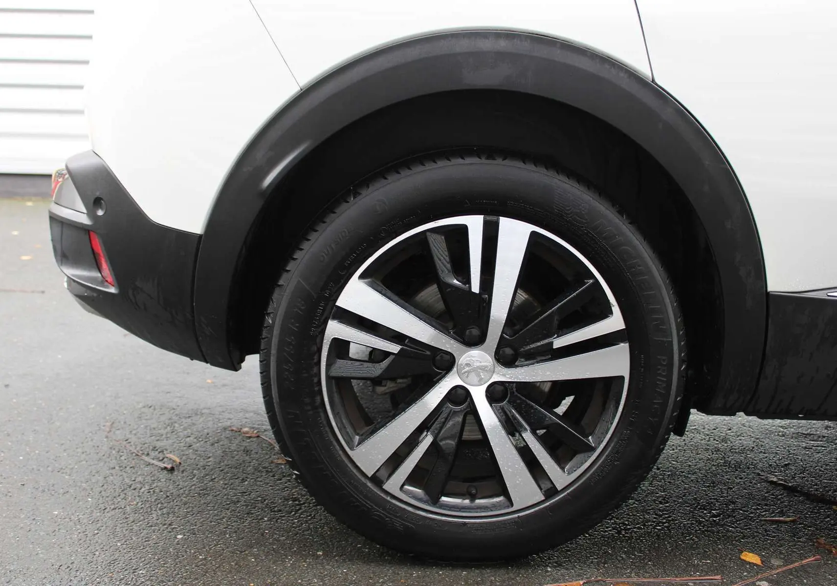 Gros plan sur la roue arrière droite du Peugeot 3008 blanc nacré 2025 avec jante alliage bicolore moderne.