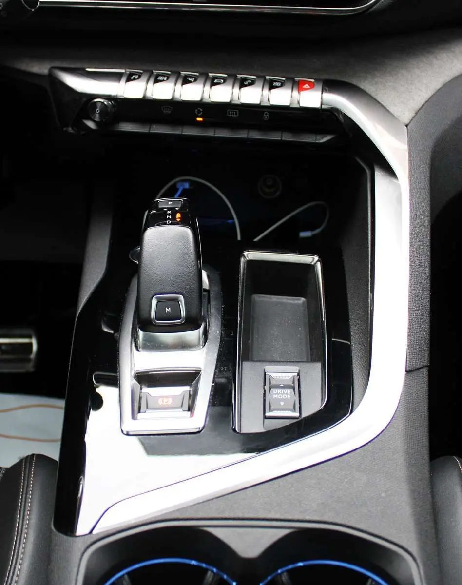 Gros plan sur la console centrale noire brillante du Peugeot 3008 2025 avec levier de vitesse automatique et bouton Drive Mode.