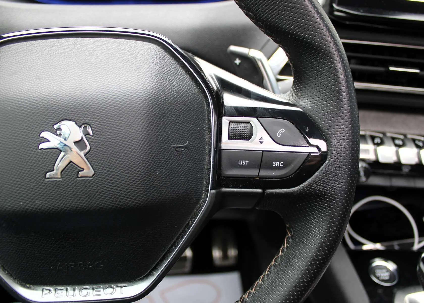 Gros plan sur le volant en cuir perforé noir du Peugeot 3008 2025 avec commandes intégrées et logo lion argenté.