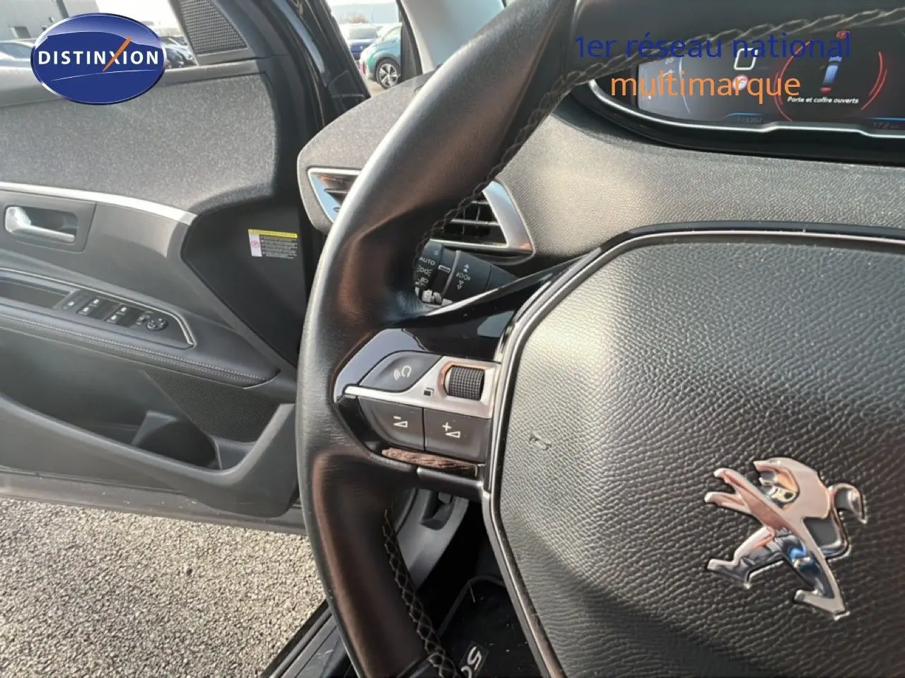 Vue intérieure côté conducteur du Peugeot 5008 noir, mettant en valeur le volant cuir avec commandes intégrées et la porte ouverte.