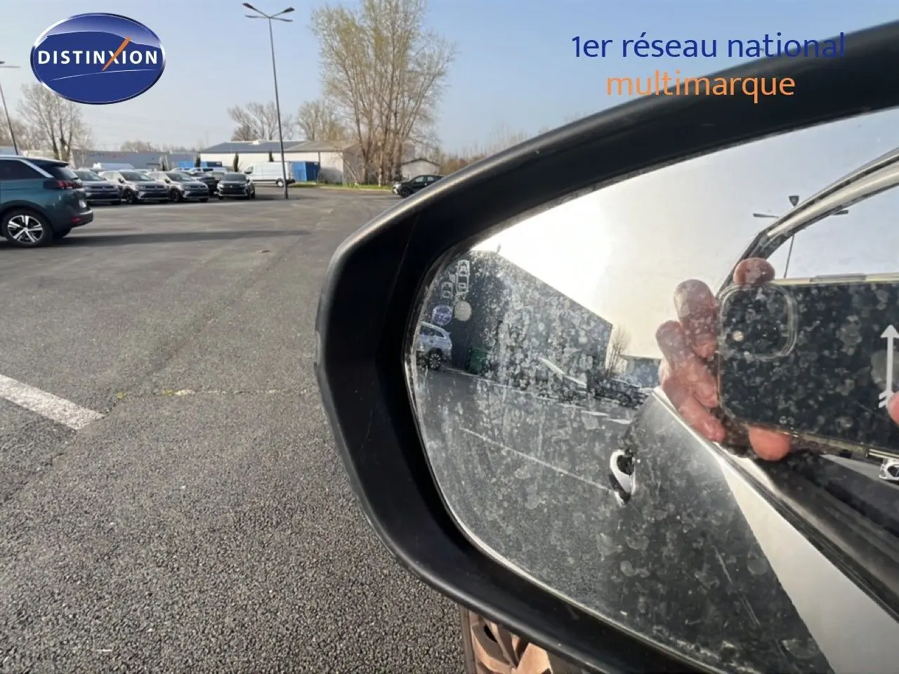 Rétroviseur latéral droit noir perla nera d’un Peugeot 5008 2018, reflet partiel du véhicule et main tenant un smartphone.