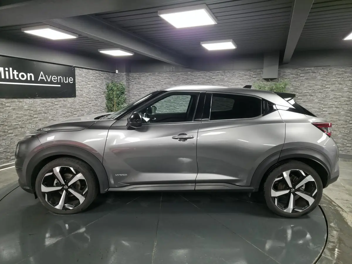 Vue latérale droite d'un Nissan Juke gris métallisé 2024 avec jantes alliage noires et grises, badge Hybrid visible.
