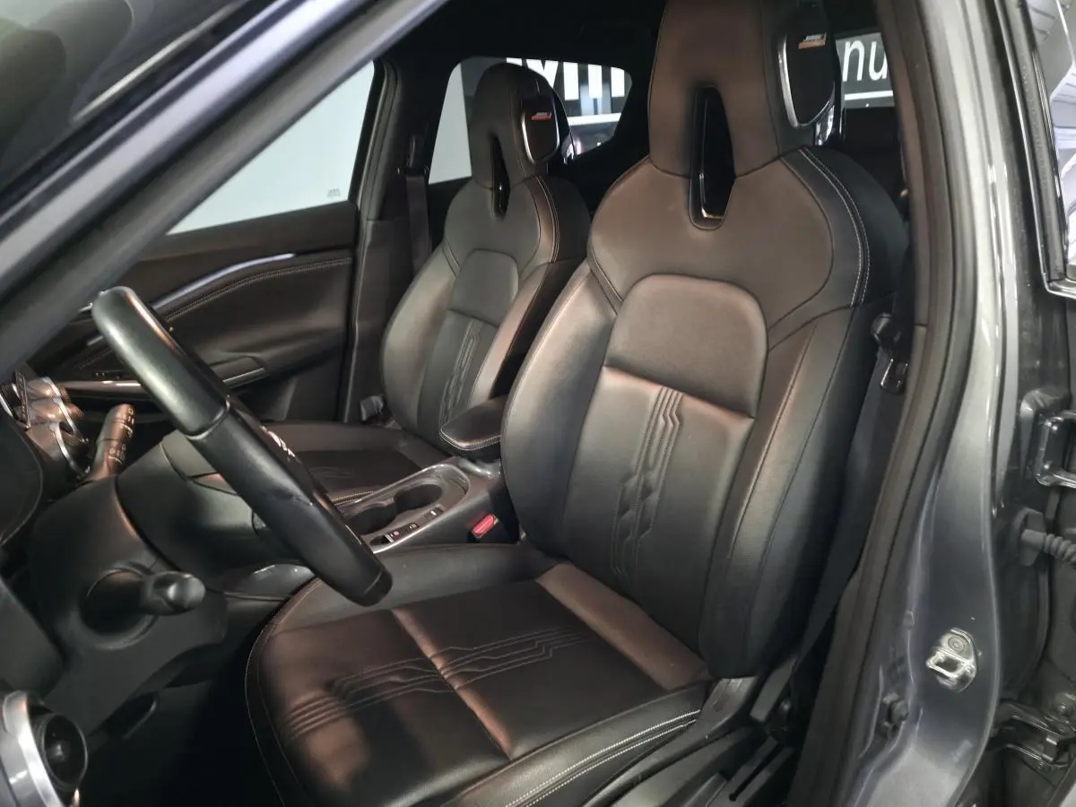 Vue intérieure côté conducteur du Nissan Juke 1.6 Hybrid 2024 avec sellerie cuir noire et accoudoir central.