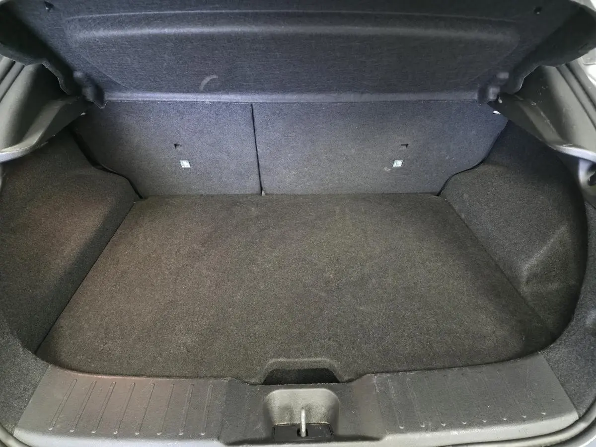 Coffre vide en vue plongeante du Nissan Juke 1.6 Hybrid gris, montrant le tapis et les parois intérieures noires.