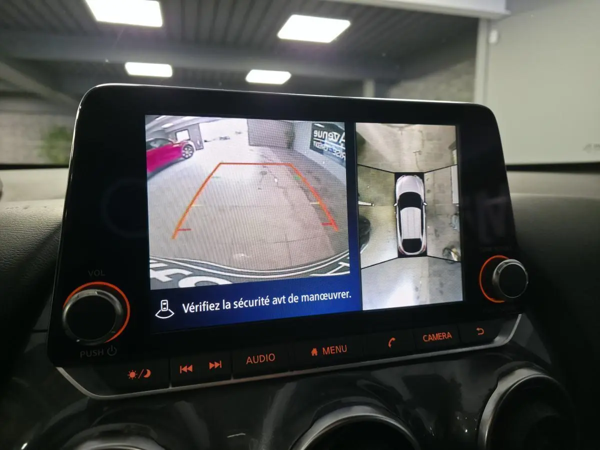 Écran multimédia affichant la caméra de recul et la vue à 360° du Nissan Juke gris en stationnement intérieur.