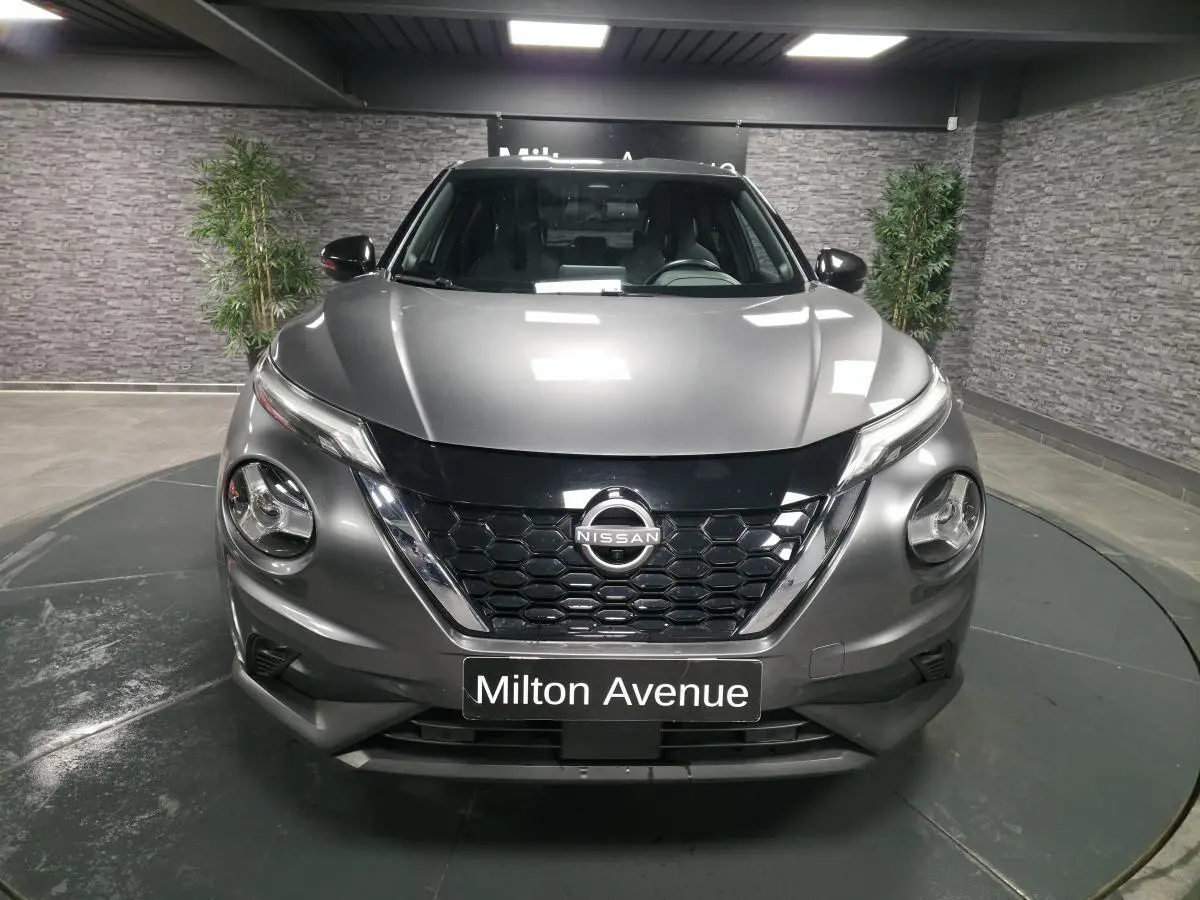 Vue avant d'un Nissan Juke gris métallisé 2024 avec calandre noire et phares LED ronds dans un showroom.