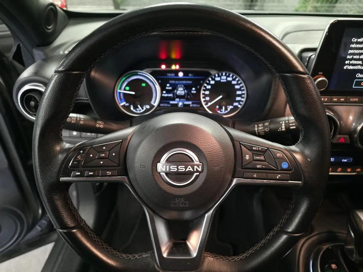 Vue rapprochée du volant cuir noir de la Nissan Juke 2024 avec commandes intégrées et tableau de bord numérique.