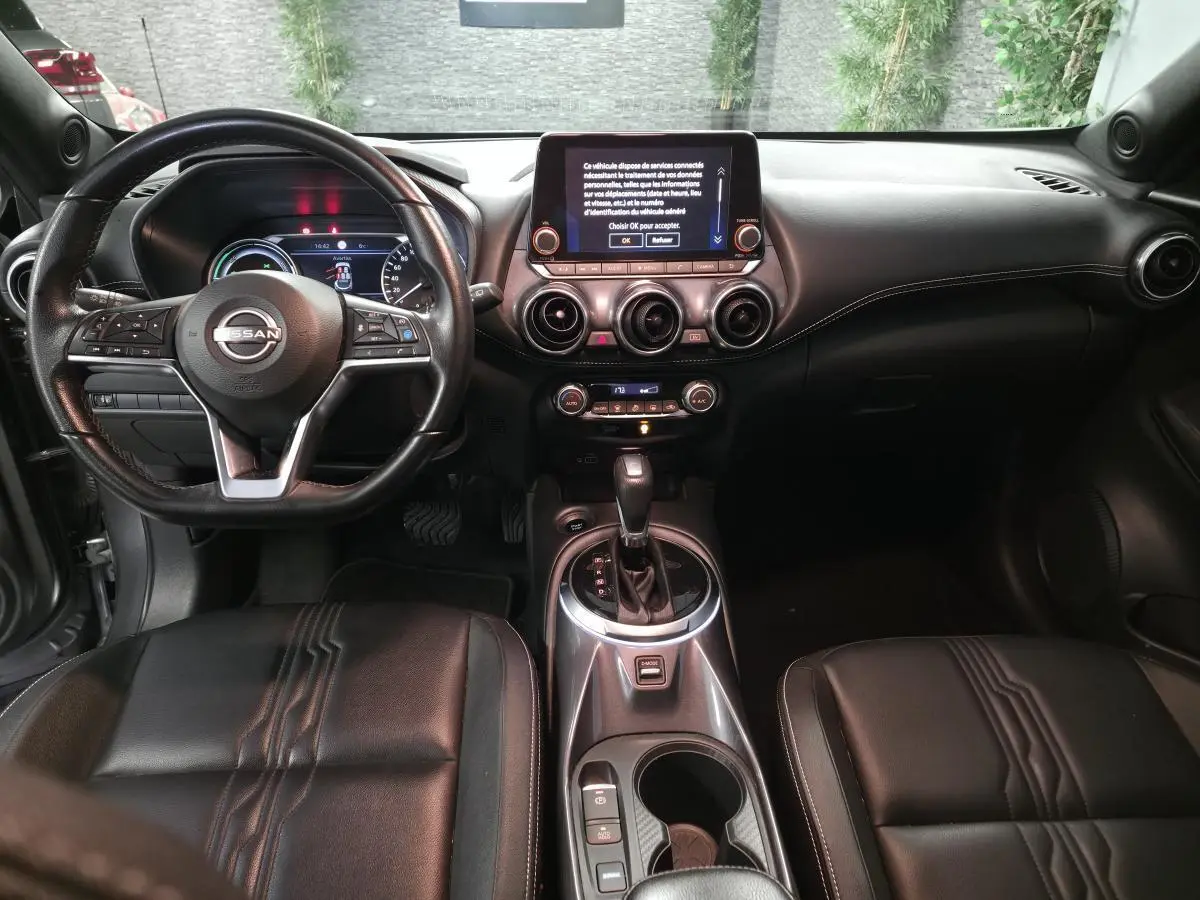 Vue intérieure avant du Nissan Juke 2024 gris, avec volant cuir, écran tactile central et sellerie cuir noire.