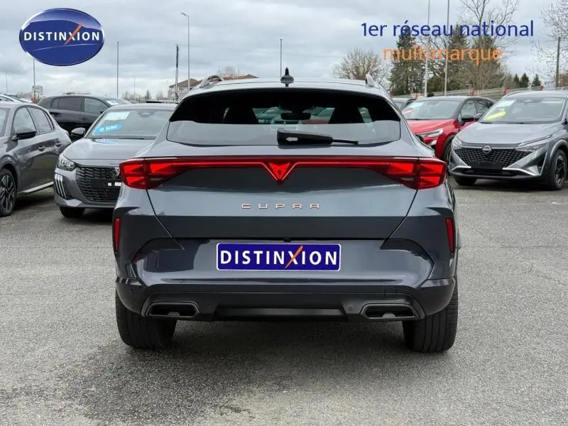 Vue arrière d'une CUPRA Formentor 1.5 eTSI Hybrid 2025 en gris magnétique mat avec feux LED reliés par une barre lumineuse rouge.