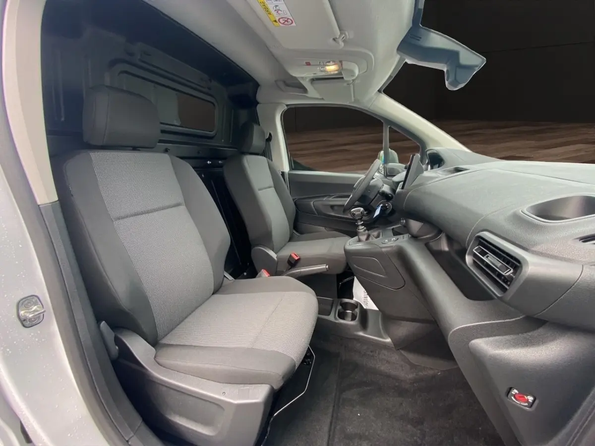 Vue intérieure côté conducteur du Peugeot Partner blanc 2024, montrant les sièges avant gris et le tableau de bord moderne.