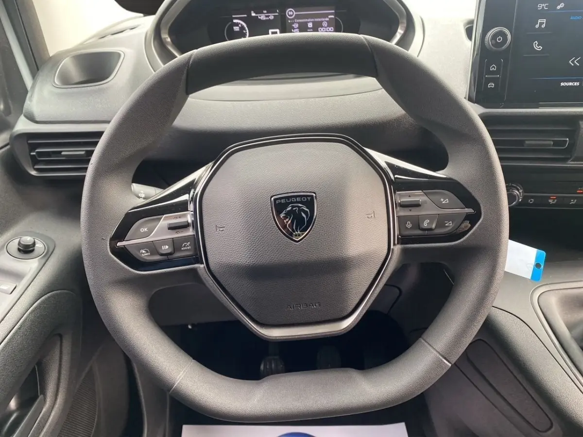 Vue rapprochée du volant multifonctions Peugeot noir dans l’habitacle du Partner 2024 avec tableau de bord et écran tactile.