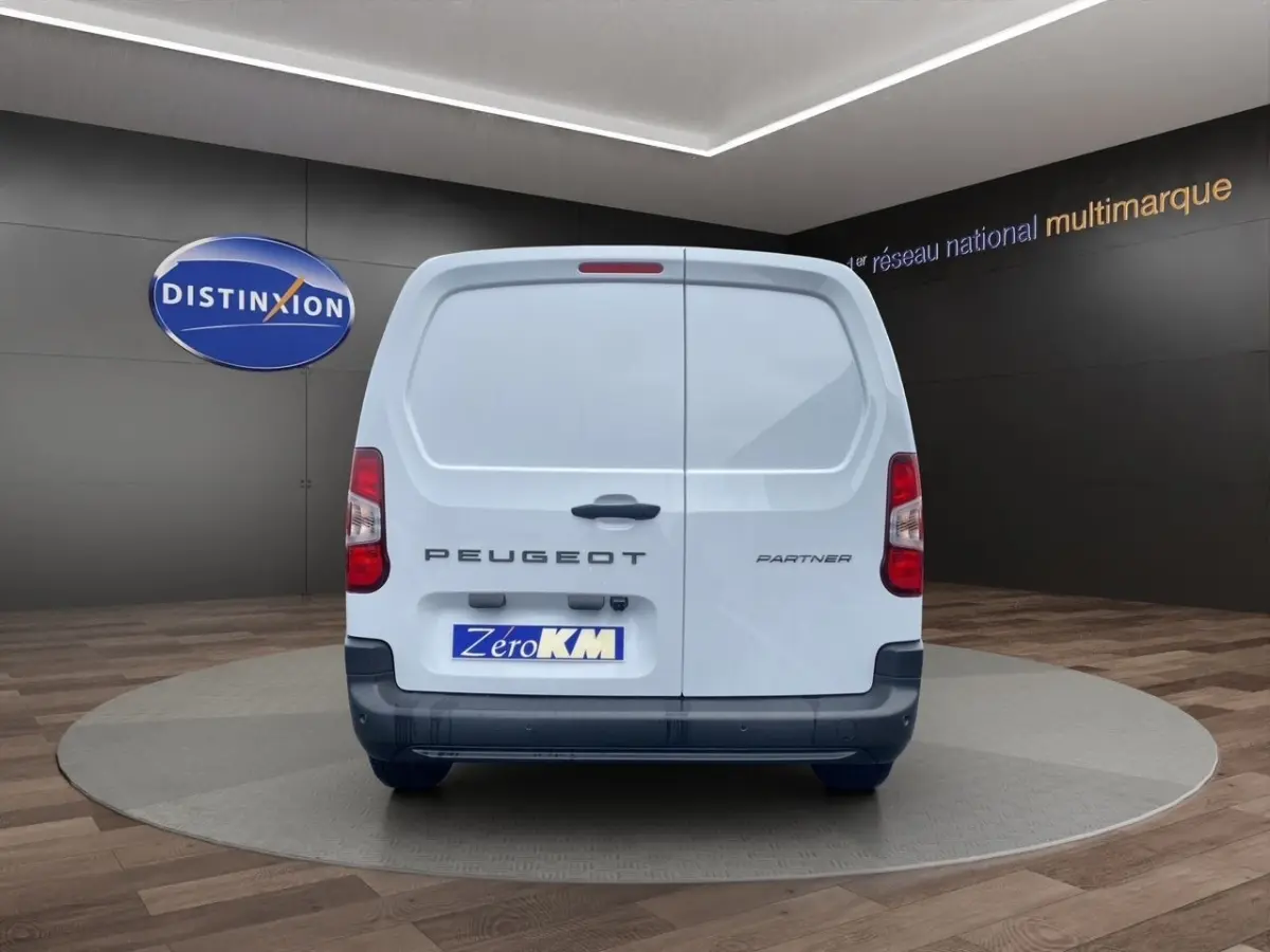 Vue arrière d’un utilitaire blanc Peugeot Partner 2024 sur plateau tournant en showroom.