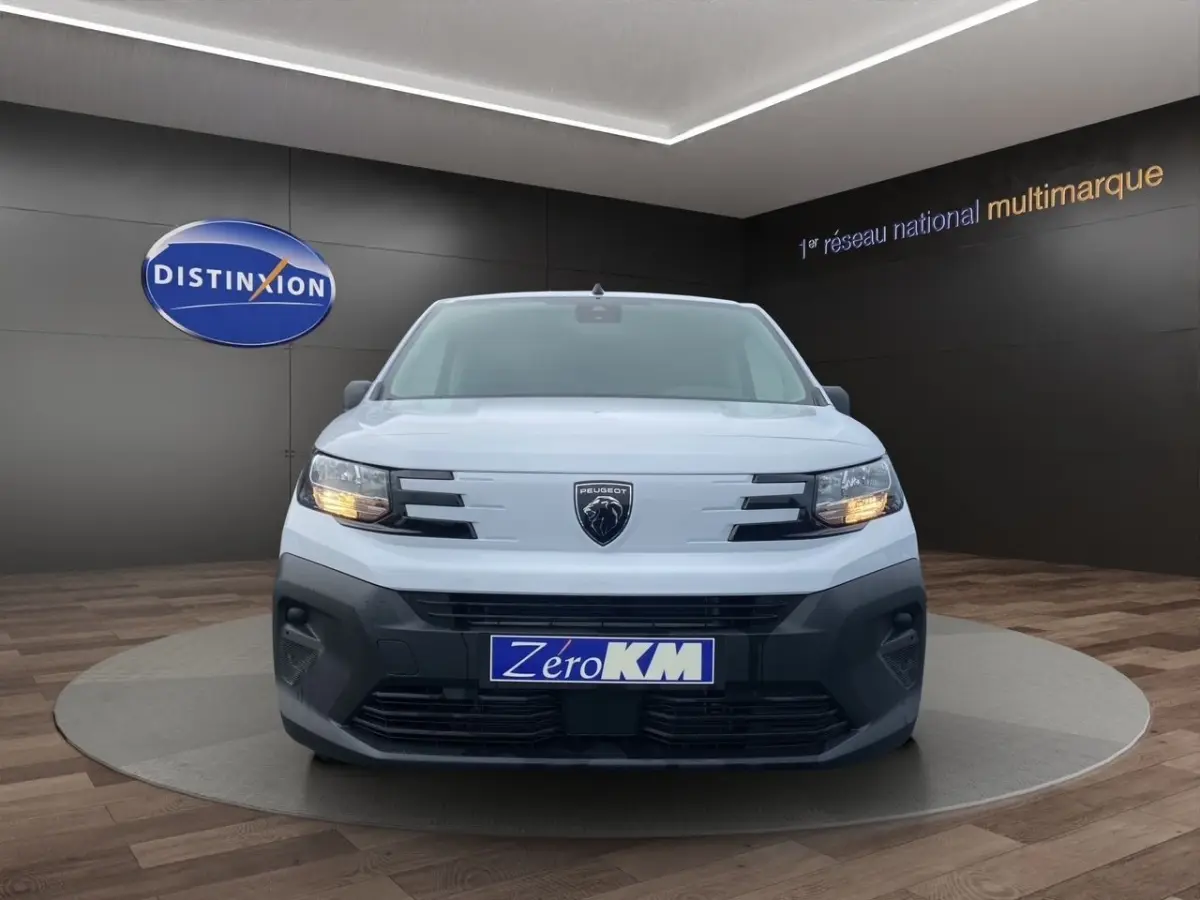 Vue avant du Peugeot Partner blanc 2024 avec phares allumés et calandre noire distinctive.