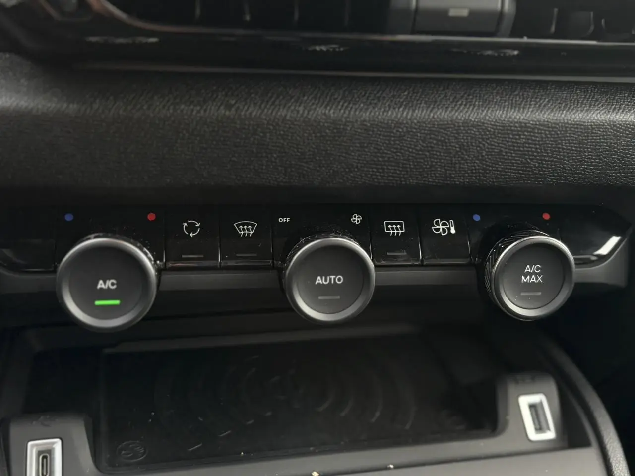 Gros plan sur la console centrale noire du Citroën C4 Hybrid 2025 avec commandes de climatisation et recharge sans fil.