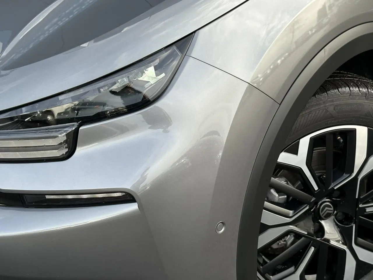 Gros plan sur l'avant droit gris Mercury du Citroën C4 Hybrid 2025, mettant en valeur le phare LED et la jante alliage 18 pouces.