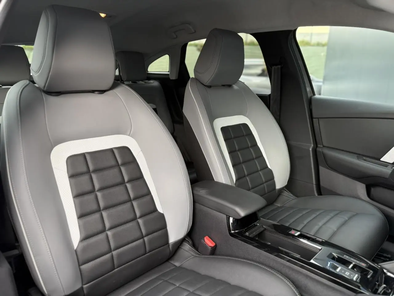 Vue intérieure des sièges avant gris clair et noir avec accoudoir central et garnitures modernes du Citroën C4 Hybrid 2025.