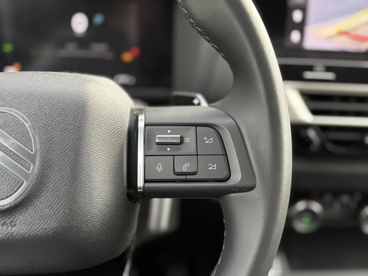 Gros plan sur les commandes du volant à droite du Citroën C4 Hybrid 2025, intérieur noir avec écran tactile en arrière-plan.