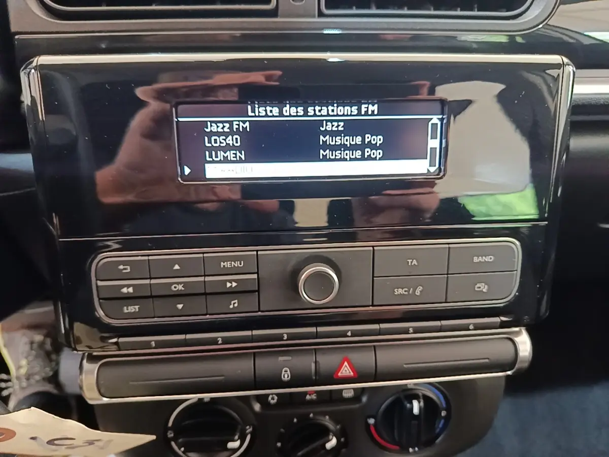 Vue rapprochée du tableau de bord noir de la Citroën C3 avec écran radio affichant la liste des stations FM.