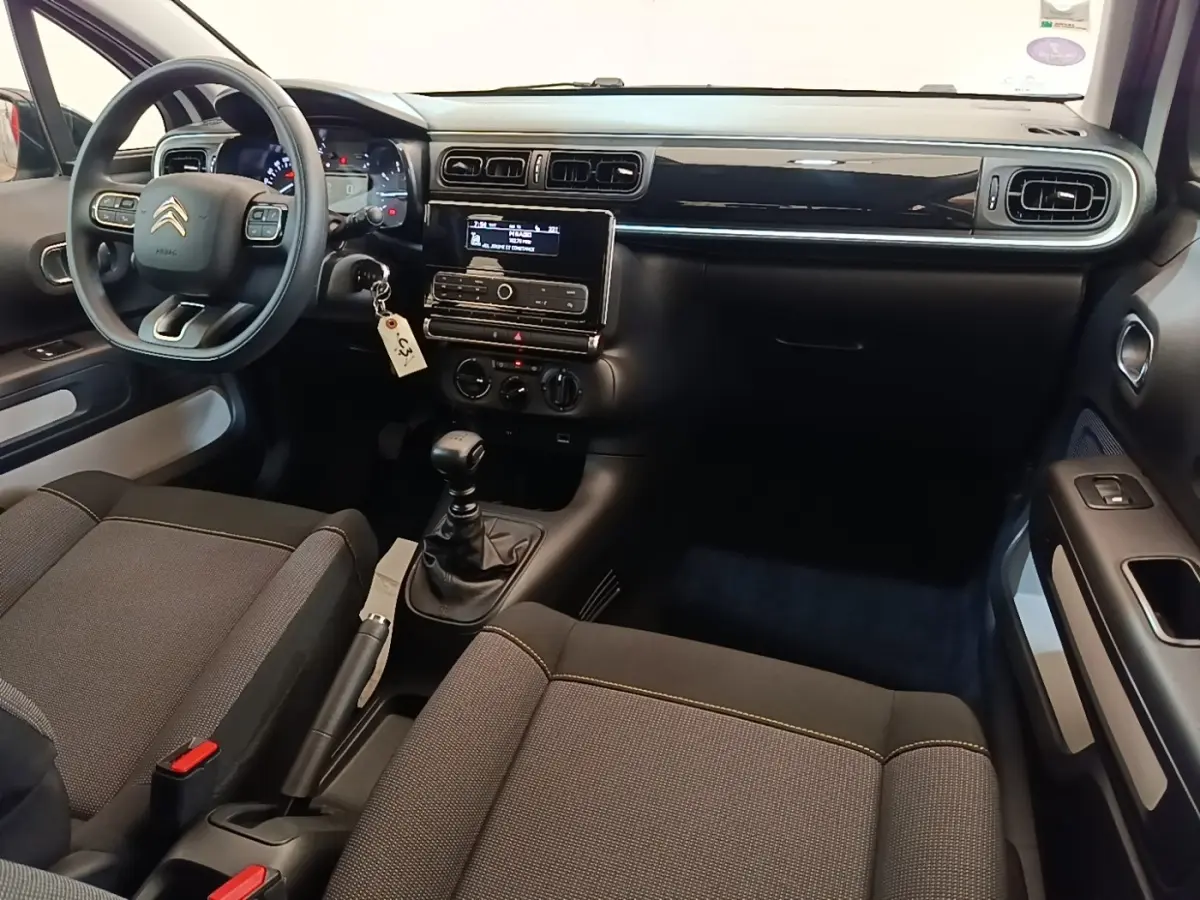 Vue intérieure avant droite du tableau de bord noir brillant et des sièges gris foncé de la Citroën C3 PureTech 110.