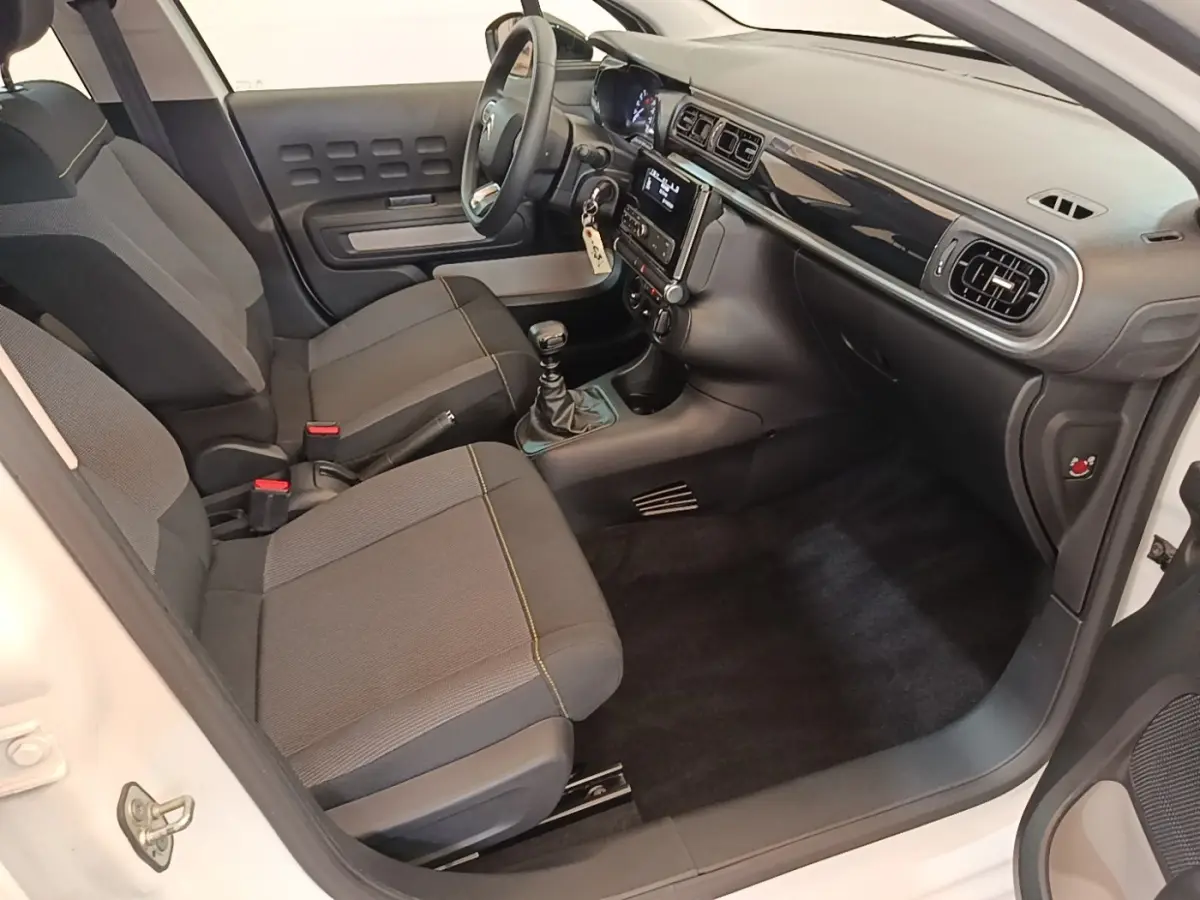 Vue intérieure côté conducteur de la Citroën C3 blanche, montrant sièges gris, volant multifonctions et tableau de bord moderne.