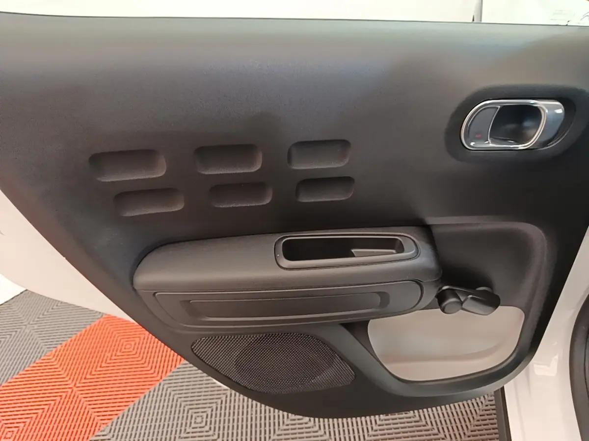 Vue rapprochée de la porte intérieure côté droit de la Citroën C3 blanche, avec poignée et commande de vitre manuelle.