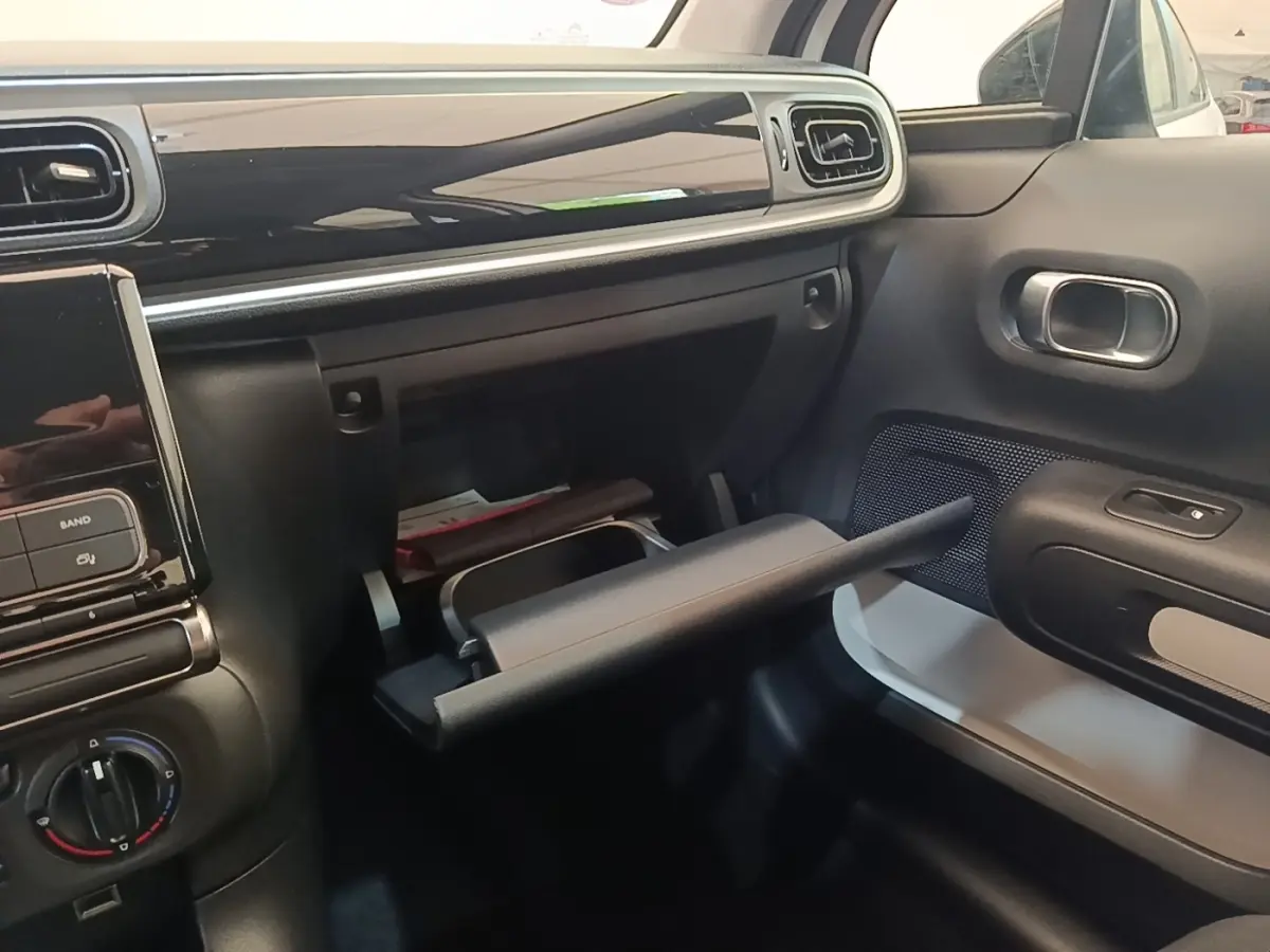 Intérieur de la Citroën C3 blanc, vue côté passager sur la boîte à gants ouverte et tableau de bord noir brillant.