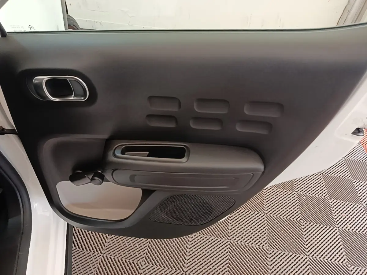 Vue intérieure du panneau de porte avant gauche noir de la Citroën C3 blanche de 2019, avec poignée et haut-parleur intégrés.