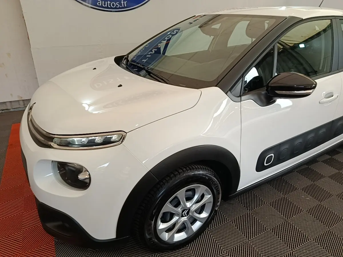 Vue 3/4 avant droit d'une Citroën C3 blanche avec protections latérales noires et jantes alliage argentées.