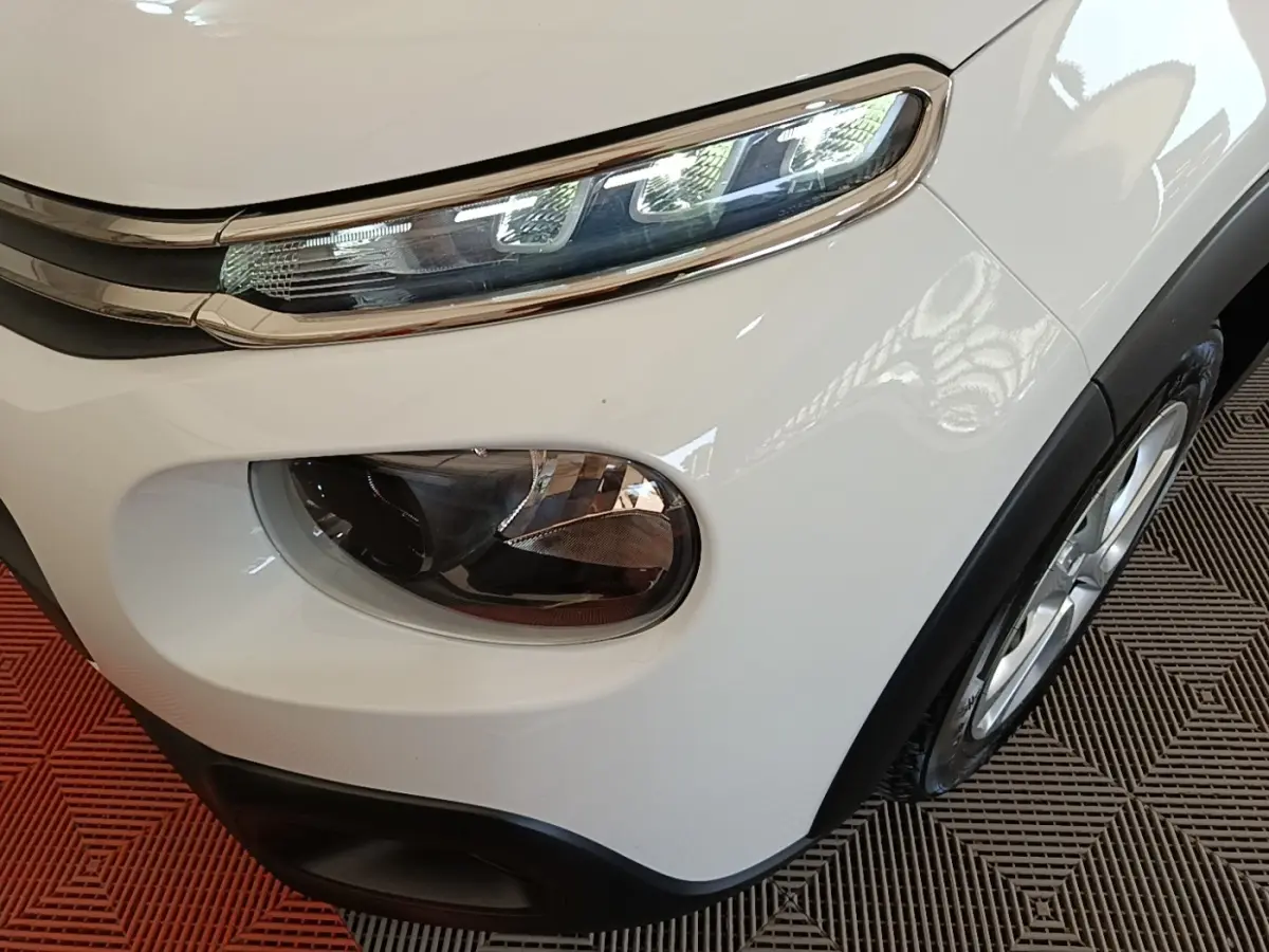 Gros plan sur l'avant droit blanc d'une Citroën C3 2019, mettant en valeur ses phares distinctifs et la roue.