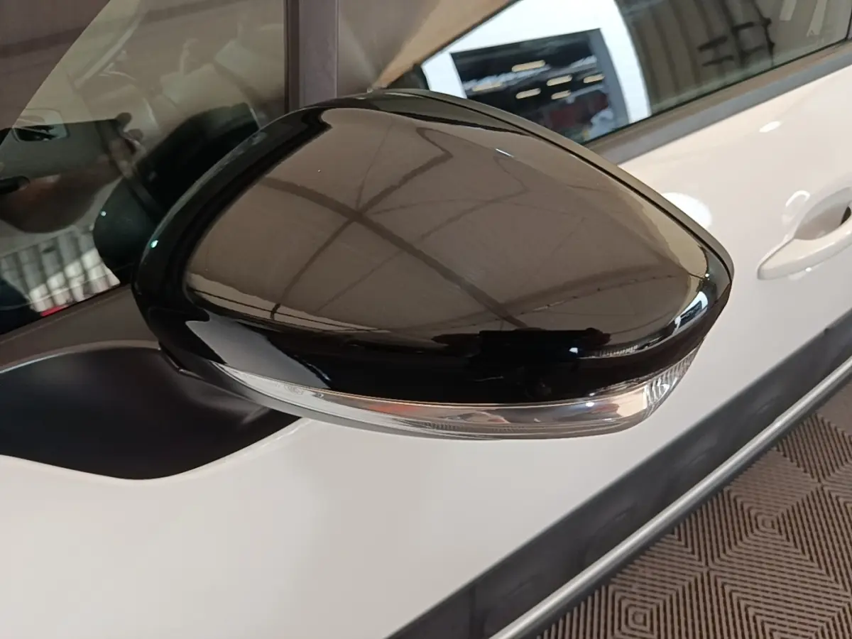 Gros plan sur le rétroviseur droit noir brillant d'une Citroën C3 blanche, avec poignée de porte visible en arrière-plan.