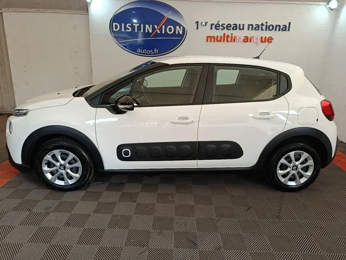 Profil droit d'une Citroën C3 blanche 2019 avec protections latérales noires et jantes argentées en intérieur showroom.
