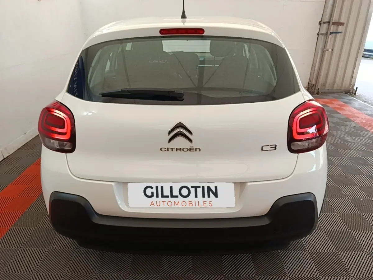 Vue arrière d'une Citroën C3 blanche de 2019 avec feux arrière allumés et pare-chocs noir dans un garage.