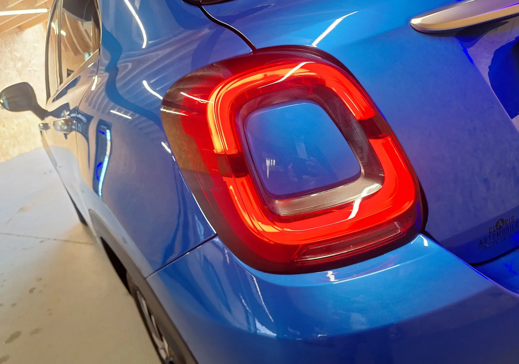 Gros plan sur le feu arrière droit rouge d'une FIAT 500X 2024 bleu métallisé, avec reflet intérieur visible.