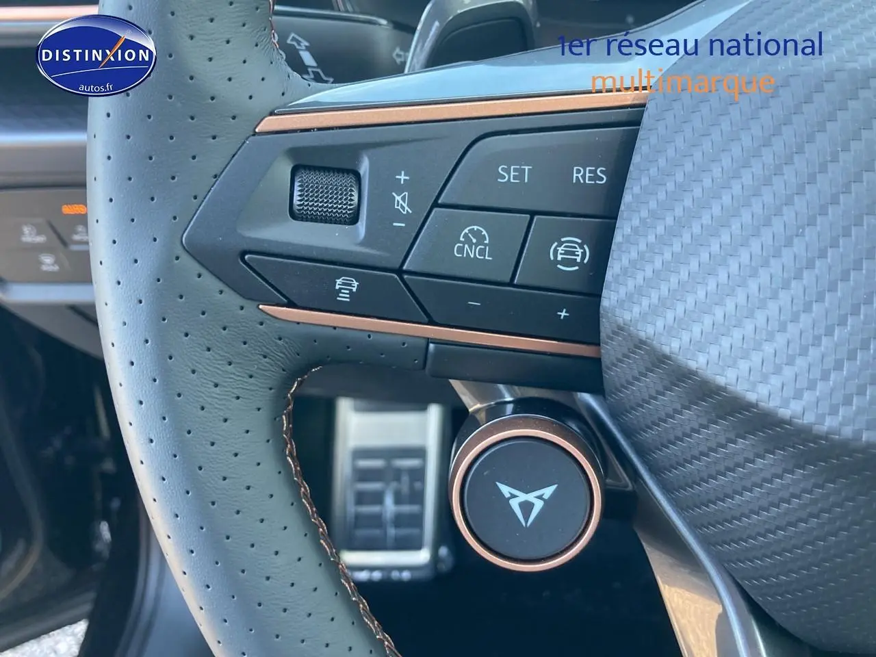 Gros plan sur le volant cuir perforé noir avec commandes multifonctions et logo CUPRA au centre.