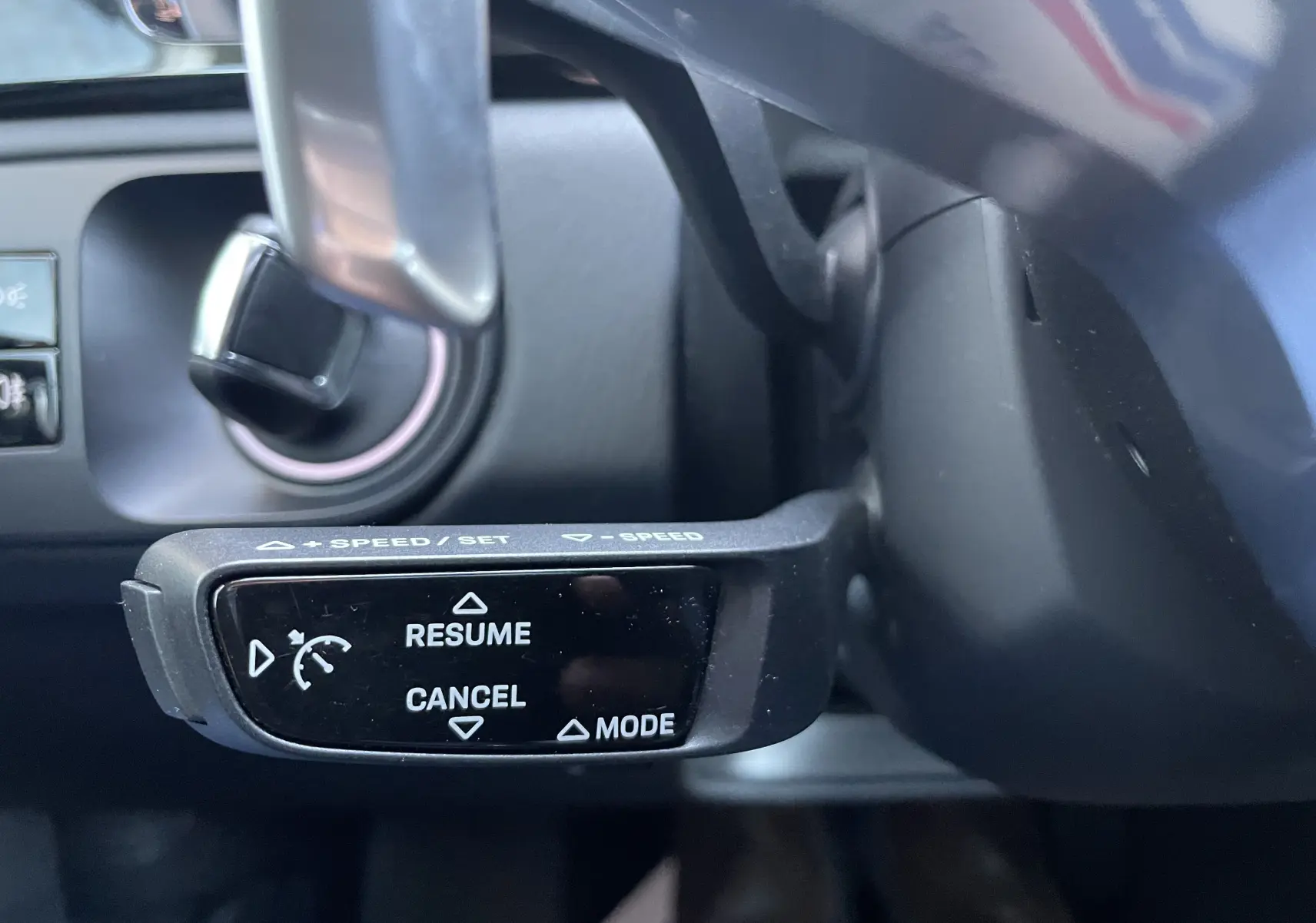 Gros plan sur la commande de régulateur de vitesse au volant d’un Porsche Cayenne gris Kerguelen 2018 hybride rechargeable.