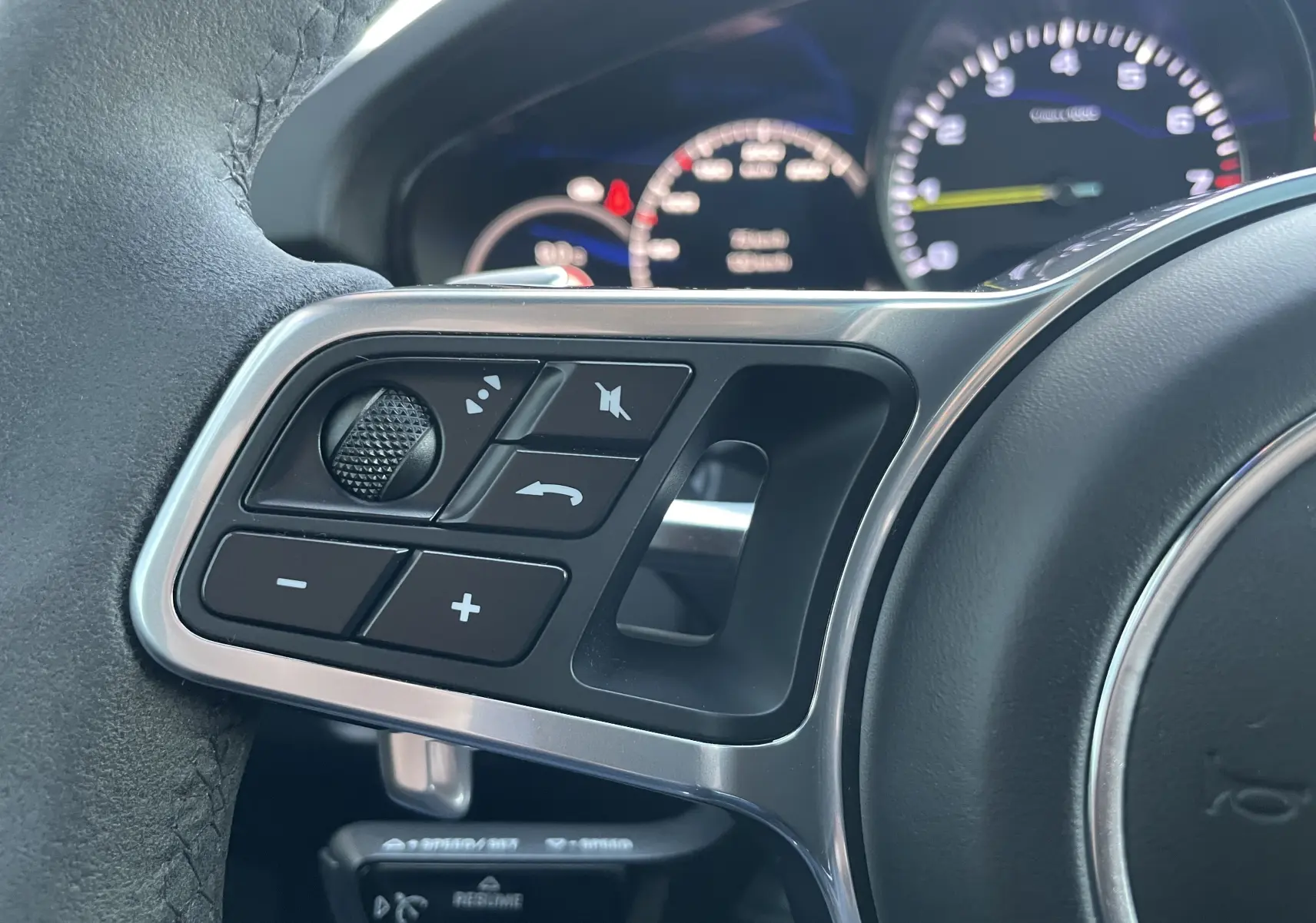 Gros plan sur les commandes gauche du volant du Porsche Cayenne E-Hybrid gris, avec tableau de bord en arrière-plan flou.