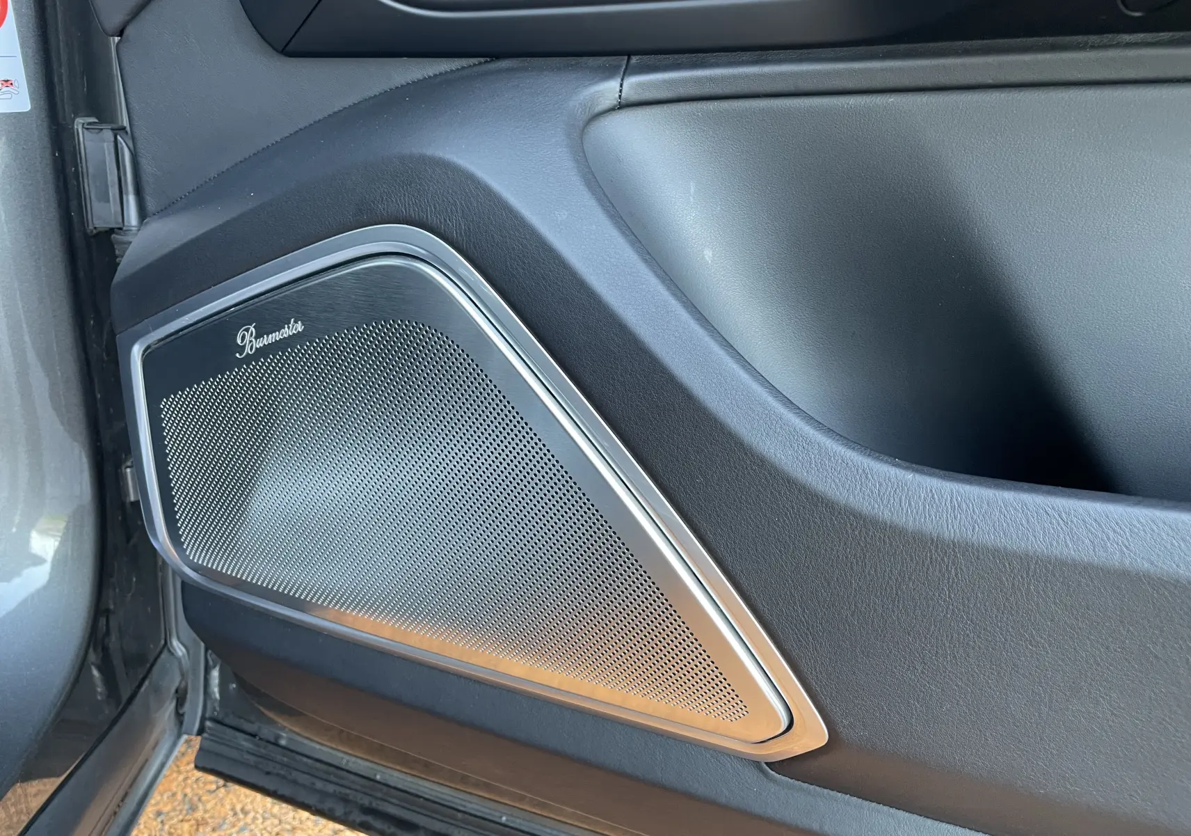 Gros plan sur l'enceinte Burmester intégrée à la porte côté gauche d'un Porsche Cayenne E-Hybrid gris Kerguelen 2018.