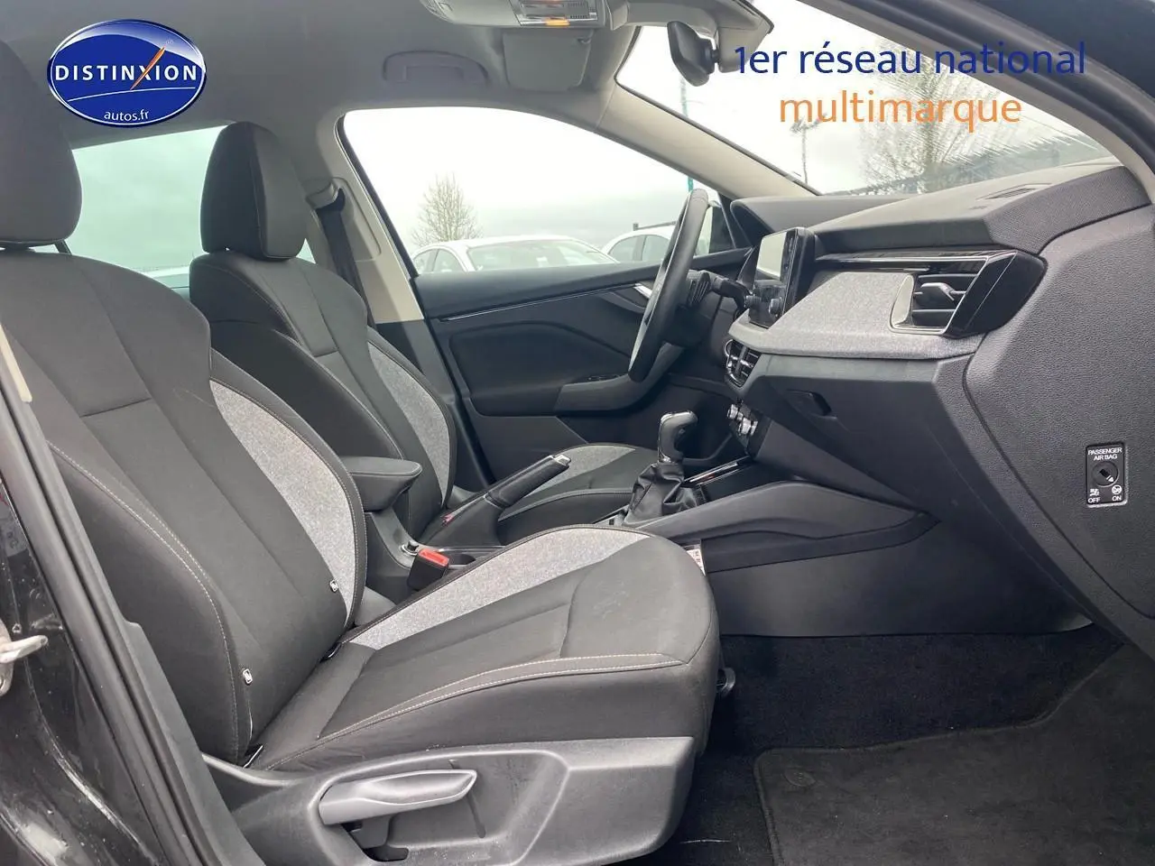 Vue intérieure côté gauche du poste de conduite du Skoda Kamiq noir 2025, avec sièges tissu bicolore et tableau de bord moderne.