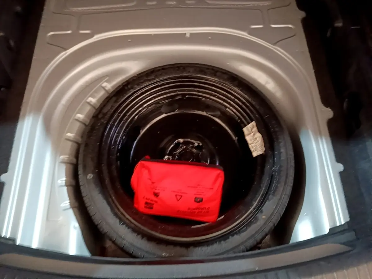 Gros plan sur la roue de secours galette noire dans le coffre d’une SEAT LEON gris foncé, avec trousse de secours rouge.